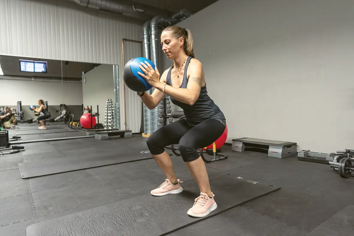 Frau macht Kniebeugen mit einem Medizinball auf der Trainingsfläche